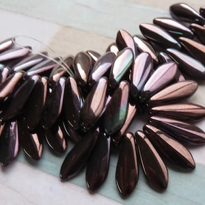 May include: A collection of iridescent brown glass beads in a teardrop shape. The beads have a metallic sheen and are arranged in a fan shape.