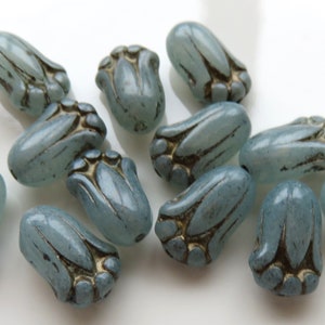 May include: A collection of 12 light blue glass beads with a flower design. The beads have a frosted finish and are accented with a metallic silver color.