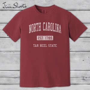 K&ouml;nnte beinhalten: Ein weinrotes T-Shirt mit dem wei&szlig;en Schriftzug "NORTH CAROLINA" oben. Darunter steht "EST. 1789" und "TAR HEEL STATE" im Vintage-Stil. Das T-Shirt hat kurze &Auml;rmel und einen Rundhalsausschnitt.