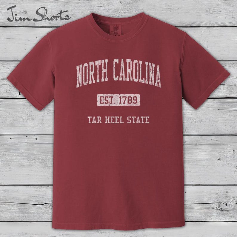 K&ouml;nnte beinhalten: Ein weinrotes T-Shirt mit dem wei&szlig;en Schriftzug "NORTH CAROLINA" oben. Darunter steht "EST. 1789" und "TAR HEEL STATE" im Vintage-Stil. Das T-Shirt hat kurze &Auml;rmel und einen Rundhalsausschnitt.