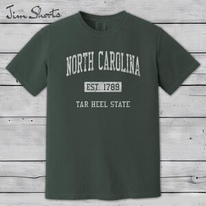 K&ouml;nnte beinhalten: Dunkelgr&uuml;nes T-Shirt mit dem Schriftzug "North Carolina" in verblichener wei&szlig;er Schrift. Darunter steht "Est. 1789" und "Tar Heel State". Das T-Shirt hat einen Rundhalsausschnitt und kurze &Auml;rmel.