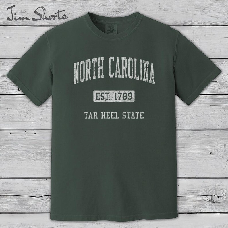 K&ouml;nnte beinhalten: Dunkelgr&uuml;nes T-Shirt mit dem Schriftzug "North Carolina" in verblichener wei&szlig;er Schrift. Darunter steht "Est. 1789" und "Tar Heel State". Das T-Shirt hat einen Rundhalsausschnitt und kurze &Auml;rmel.