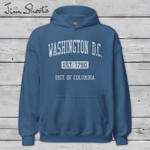 May include: A blue hoodie with the text "WASHINGTON D.C." in white, along with "EST. 1790" and "DIST. OF COLUMBIA." The hoodie has a front pocket and a hood. The brand name "Jim Shorts" is in the top left corner.