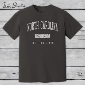 K&ouml;nnte beinhalten: Dunkelgraues T-Shirt mit dem Schriftzug "North Carolina" in verblichener wei&szlig;er Schrift. Darunter steht "Est. 1789" und "Tar Heel State". Das Shirt hat kurze &Auml;rmel und einen Rundhalsausschnitt.