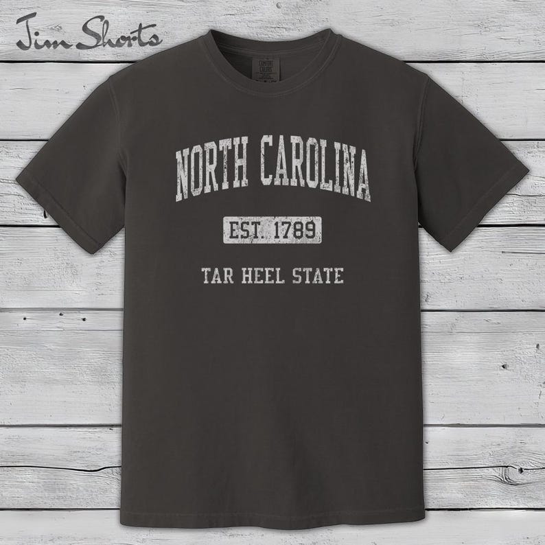 K&ouml;nnte beinhalten: Dunkelgraues T-Shirt mit dem Schriftzug "North Carolina" in verblichener wei&szlig;er Schrift. Darunter steht "Est. 1789" und "Tar Heel State". Das Shirt hat kurze &Auml;rmel und einen Rundhalsausschnitt.
