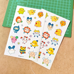 May include: Two sheets of stickers featuring colorful cartoon characters. The stickers include various designs of cute creatures in different shapes and colors, such as yellow ducks, blue robots, and pink creatures. The text "@hghostt" is visible on one sheet.
