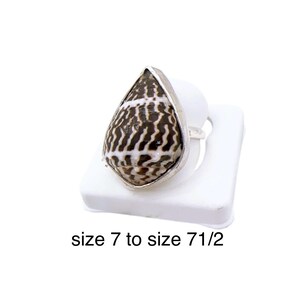 Peut inclure: Bague en argent ornée d'un coquillage en forme de goutte d'eau, avec un motif brun et blanc. La bague est présentée sur un support blanc. Le texte sur l'image indique "size 7 to size 7 1/2".