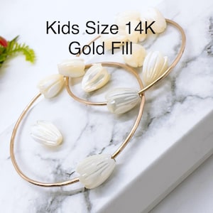 May include: Two gold-filled bracelets with white shell flower charms. The bracelets are labeled "Kids Size 14K Gold Fill".