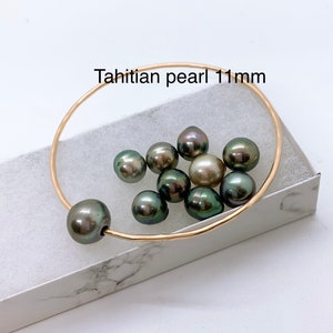 Peut inclure: Un bracelet jonc en or avec un groupe de perles de Tahiti vert foncé et or, mesurant 11 mm de diamètre. Les perles sont disposées en un motif lâche et organique, et le bracelet est ouvert et prêt à être porté.