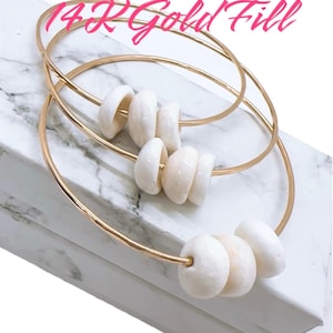 May include: Two gold bangles with white shell beads. The bangles are 14K gold filled.