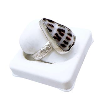 Peut inclure: Bague en argent ornée d'un coquillage en forme de goutte d'eau, orné de motifs noirs et blancs. Le coquillage est serti dans une lunette en argent. L'anneau de la bague présente un motif floral.