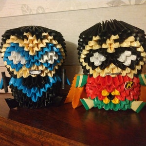 May include: Two origami figures of Batman and Robin. Batman is blue, black and white. Robin is red, yellow, green, black and white. Robin has the letter "R" on his chest.