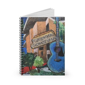 Op de afbeelding: Spiraalgebonden notitieboek met een kleurrijke illustratie. De omslag toont een blauwe gitaar, een gebouw en een bord met de tekst "Pontevedra Concert Halle". Het notitieboek heeft gelinieerde pagina's.