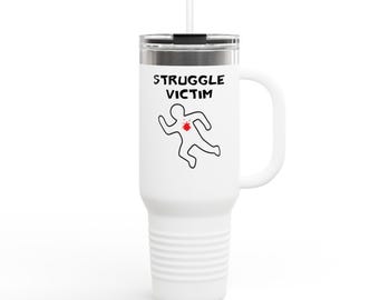 May include: White travel mug with a black lid, handle, and straw. The mug features the text "STRUGGLE VICTIM" above a black outline of a body with a red splatter. The mug is designed to keep drinks hot or cold.