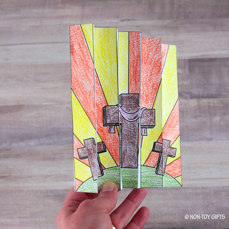 May include: A paper craft with three crosses, one larger than the others, against a background of orange and yellow rays. The crosses are brown and the largest cross has a purple cloth draped over it.