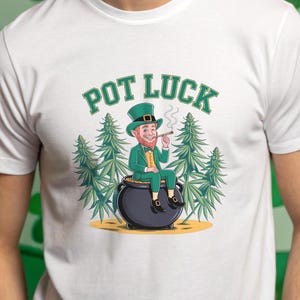May include: A white t-shirt with a green leprechaun cartoon character sitting on a pot of gold. The leprechaun is wearing a green hat and holding a cigar. The text "POT LUCK" is printed in green above the character.