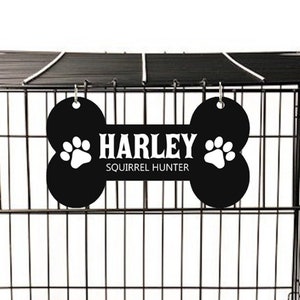 May include: Black dog crate with a black bone-shaped name tag that says "Harley Squirrel Hunter" hanging from the top.