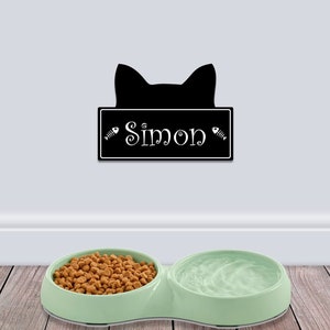 May include: A green double cat bowl with a black cat silhouette and the name "Simon" on a black sign above it.