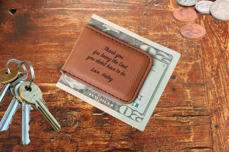 Puede incluir: Un clip de dinero de cuero marr&oacute;n con el texto "Gracias por ser el pap&aacute; que no ten&iacute;as que ser. Con amor, Haley" grabado en &eacute;l. El clip de dinero est&aacute; sobre un billete de veinte euros.