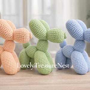 Può includere: Tre sculture di cani a palloncino all'uncinetto nei colori pastello: pesca, verde e blu. I cani fatti a mano sono esposti su una superficie di legno. Il testo "LovelyTreasureNest" è visibile sull'immagine.