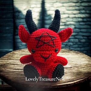 May include: A red crocheted plush toy shaped like a horned creature with black horns, black feet, and black eyes. A black pentagram is stitched onto the forehead, and the text LovelyTreasureNest is printed in white at the bottom of the image.