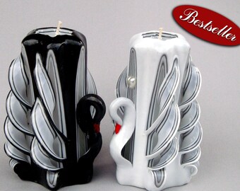May include: Two carved candles, one black and one white, each with a swan design. The black candle has a black swan with a red beak. The white candle has a white swan with a red beak and a pearl. The word "Bestseller" is in a red oval.