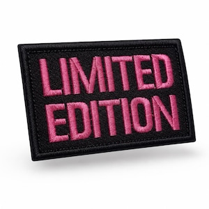 Könnte beinhalten: Ein rechteckiger, schwarz bestickter Aufnäher mit genähtem Rand. Der Text LIMITED EDITION ist in fetten, leuchtend pinkfarbenen Großbuchstaben in die Mitte des Aufnähers gestickt, was einen starken Kontrast zum schwarzen Stoffhintergrund bildet.