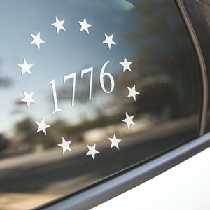 K&ouml;nnte beinhalten: Ein wei&szlig;er Autofensteraufkleber mit einem Kreis aus Sternen, der die Zahl 1776 umgibt.