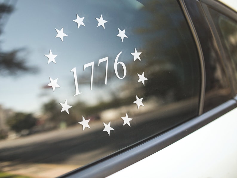 K&ouml;nnte beinhalten: Ein wei&szlig;er Autofensteraufkleber mit einem Kreis aus Sternen, der die Zahl 1776 umgibt.