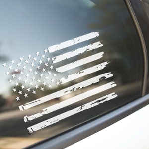 Peut inclure: Un autocollant de drapeau am&eacute;ricain blanc vieilli sur la vitre d'une voiture. Le drapeau est dans un style vieilli et d&eacute;labr&eacute;.