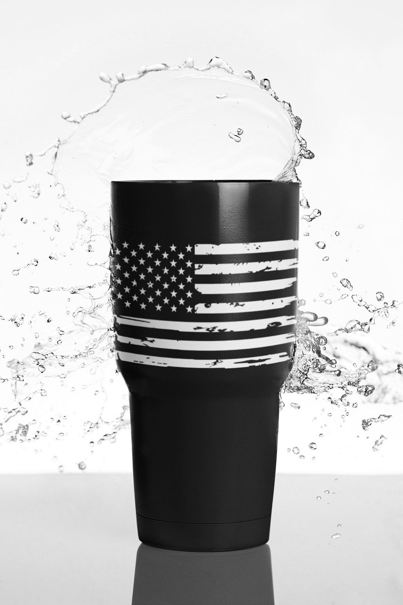 Peut inclure: Un gobelet en acier inoxydable noir avec un motif de drapeau am&eacute;ricain d&eacute;lav&eacute; blanc. Le gobelet est entour&eacute; de gouttelettes d'eau.