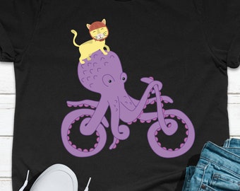 May include: A black t-shirt featuring a purple octopus riding a bicycle with a yellow cat on its head.