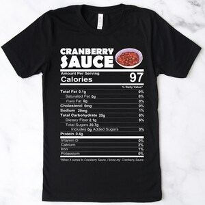 May include: Black t-shirt with a white graphic of a nutrition label for cranberry sauce. The label says "Cranberry Sauce" and lists the calories as 97. The label also includes the nutritional information for the sauce, including total fat, saturated fat, trans fat, cholesterol, sodium, total carbohydrate, dietary fiber, total sugars, protein, vitamin D, calcium, iron, and potassium.