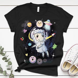 May include: Black t-shirt with a white sheep wearing an astronaut helmet floating in space. The sheep is surrounded by planets, stars, and a UFO. There are also donuts and other space-themed graphics.