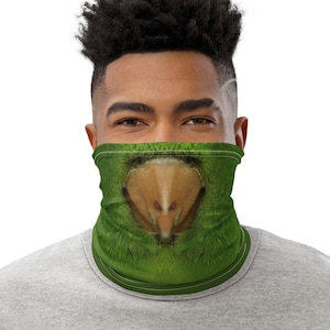 May include: Green face covering with a parrot beak design. The face covering is green with a close-up image of a parrot's beak and feathers. The face covering is worn around the neck and covers the lower face.