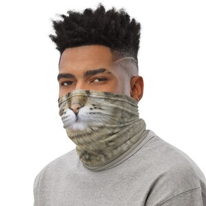 Puede incluir: Un hombre con una camisa gris y una m&aacute;scara facial con la cara de un gato. La m&aacute;scara es marr&oacute;n y gris con la nariz y los bigotes blancos.