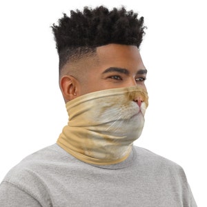 May include: A man wearing a face covering with a cat's face printed on it. The cat's face is light brown with a pink nose and white whiskers.