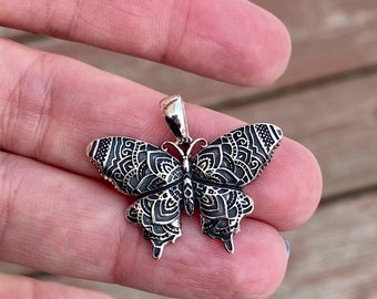 May include: Detailed silver butterfly pendant with intricate patterns on the wings. The pendant has a small loop at the top for a chain. The butterfly design is a popular jewelry theme.