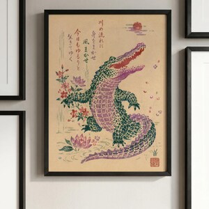 May include: A framed wall art print on tan paper featuring a green and purple crocodile with an open mouth, surrounded by pink lotus flowers and falling petals. Japanese calligraphy text is present, along with a small red sun and a red seal stamp.