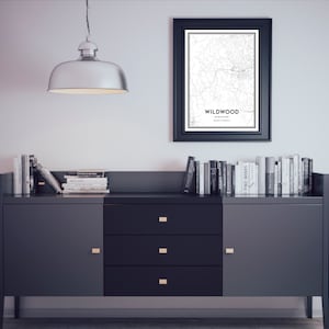 Puede incluir: Una c&oacute;moda negra con tres cajones y dos puertas. La c&oacute;moda tiene tiradores dorados. Un mapa en blanco y negro de Wildwood, Missouri enmarcado cuelga en la pared sobre la c&oacute;moda. Hay libros apilados encima de la c&oacute;moda.