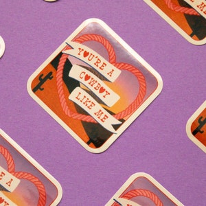 May include: A set of four square stickers with a sunset background and a rope heart design. The stickers feature the text "You're a Cowboy Like Me" with a heart symbol.