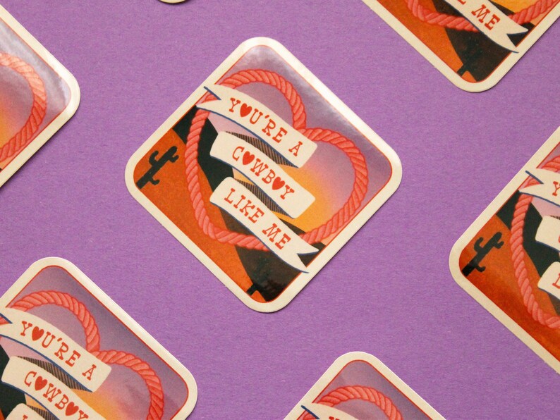 May include: A set of four square stickers with a sunset background and a rope heart design. The stickers feature the text "You're a Cowboy Like Me" with a heart symbol.