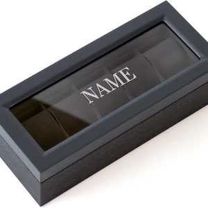 May include: Black leather watch box with a glass top and five compartments. The box is engraved with the word "NAME".