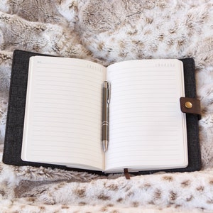 May include: An open black notebook with lined pages and a silver pen lying on a fluffy white and brown faux fur surface.