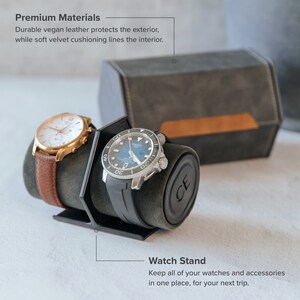 Op de afbeelding: Een horloge standaard met twee horloges, een met een bruine leren band en de andere met een zwarte rubberen band. De standaard is gemaakt van grijs vegan leer met een fluwelen interieur. De tekst "Premium Materials" en "Watch Stand" is zichtbaar in de afbeelding.