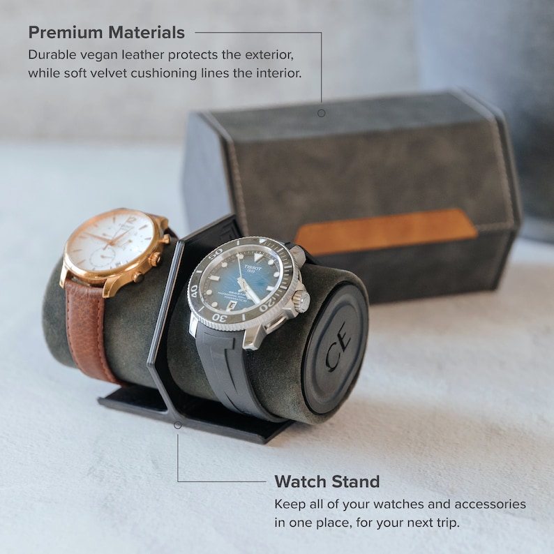 Op de afbeelding: Een horloge standaard met twee horloges, een met een bruine leren band en de andere met een zwarte rubberen band. De standaard is gemaakt van grijs vegan leer met een fluwelen interieur. De tekst "Premium Materials" en "Watch Stand" is zichtbaar in de afbeelding.