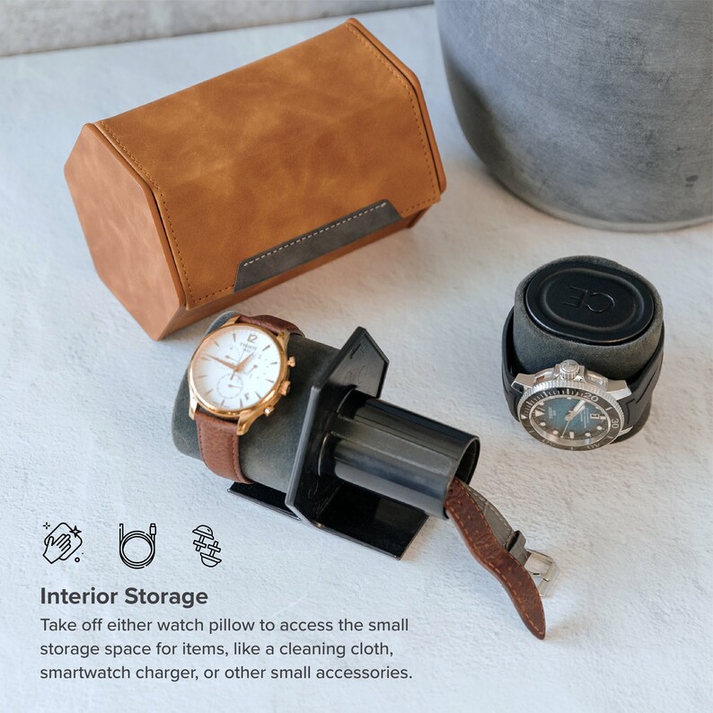 May include: A brown leather watch box with a black interior and a watch winder with a black base and a brown leather strap. The watch winder is holding a silver watch with a white face and black hands. The watch box is sitting on a white surface.