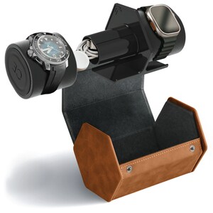 May include: A brown leather watch winder with a black interior. The winder has a built-in charging station for a smartwatch. A black and silver watch is on the winder, and a smartwatch is on the charging station.