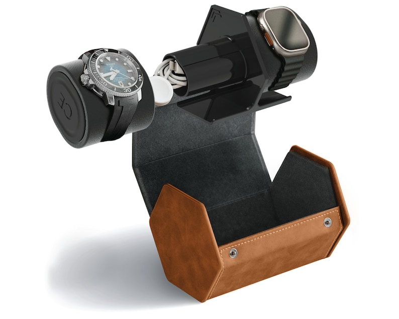 May include: A brown leather watch winder with a black interior. The winder has a built-in charging station for a smartwatch. A black and silver watch is on the winder, and a smartwatch is on the charging station.