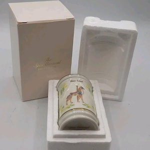 May include: A cylindrical porcelain spice jar labeled Bay Leaf with a carousel horse illustration, nestled in white styrofoam packaging next to a beige cardboard box featuring the text The Spice Carousel Fine Porcelain Collection.